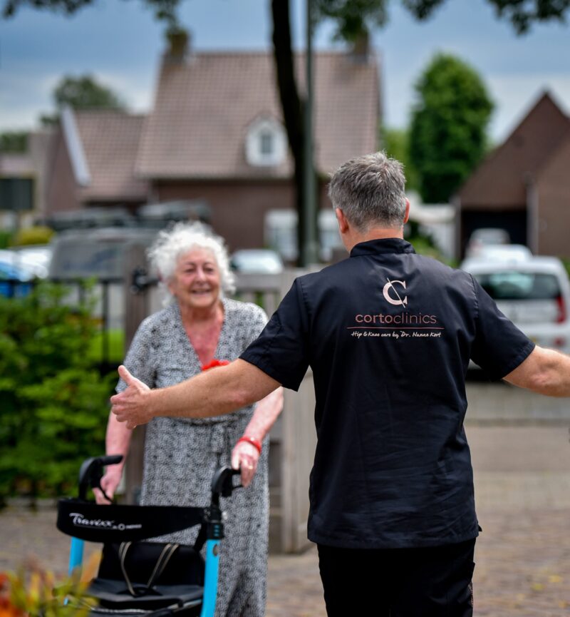 Medewerker van CortoClinics begroet een cliënt met rollator